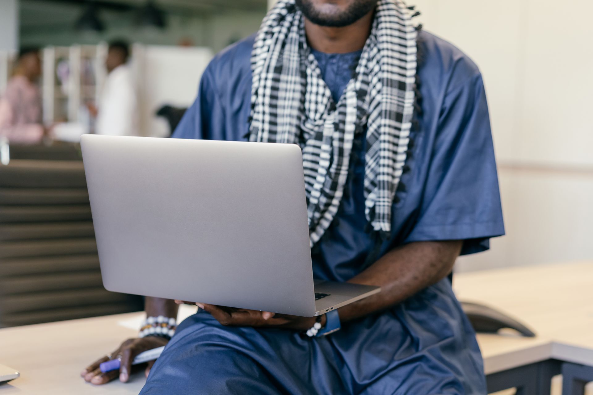 An African professional in traditional dress working on a laptop in a modern office