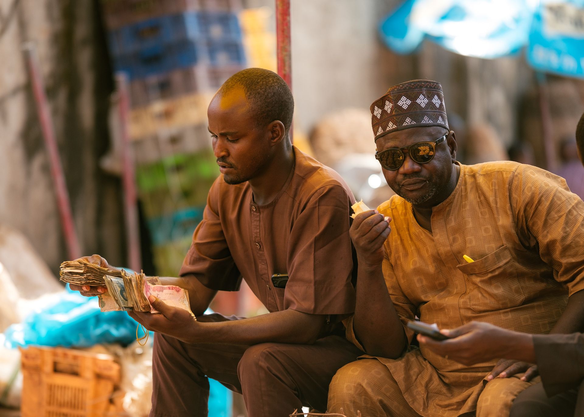Two Nigerian men in traditional dress counting naira notes at a market stall